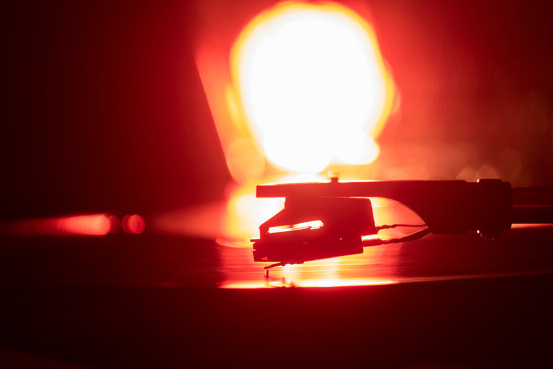 Nahaufnahme einer Plattenspielernadel auf einer Schallplatte in orangefarbenem Licht