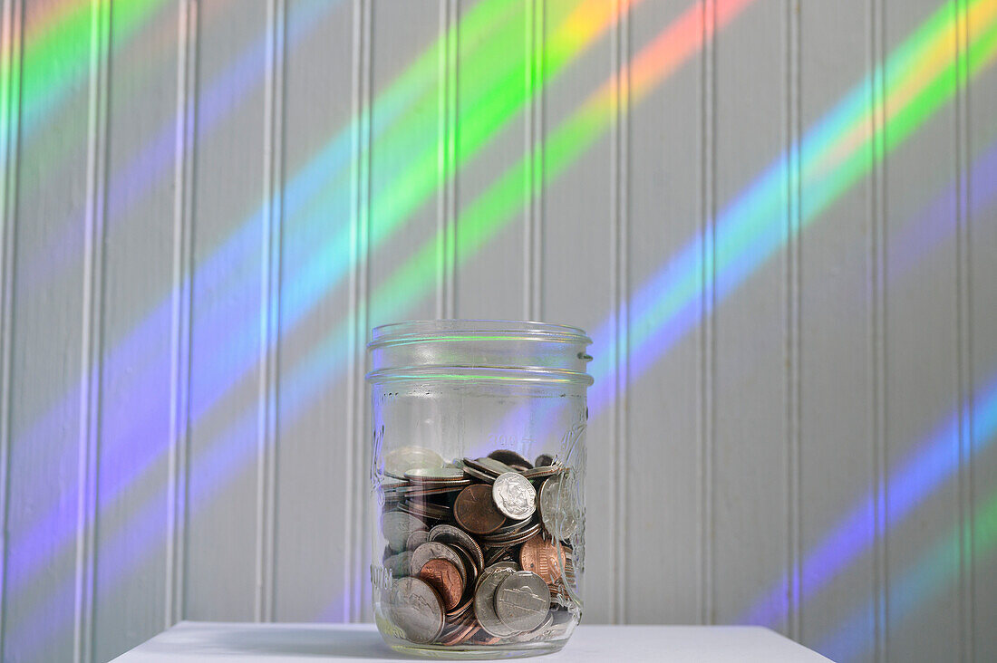 Glas mit Münzen mit Regenbogenlicht
