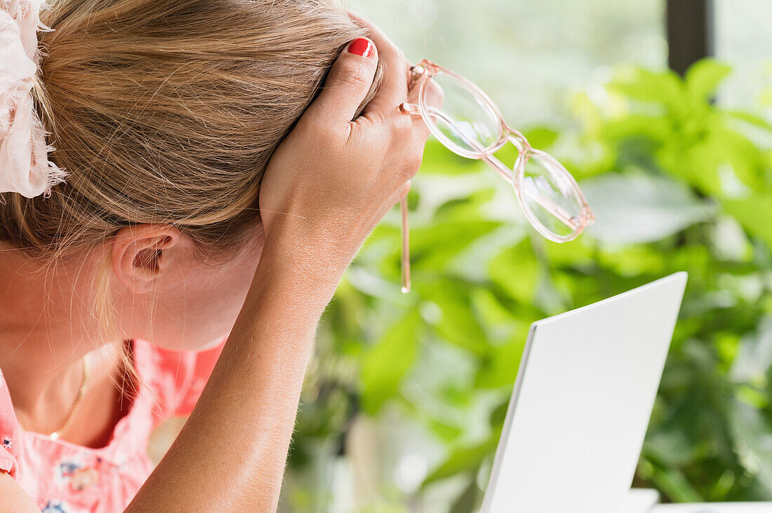 Close-up of woman with head in hands at laptop