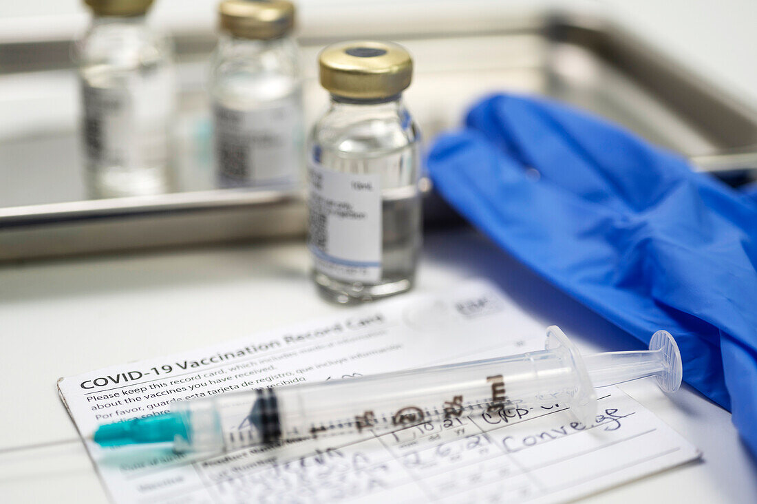 Spritze auf Covid-19-Impfausweis und Ampullen auf Tablett