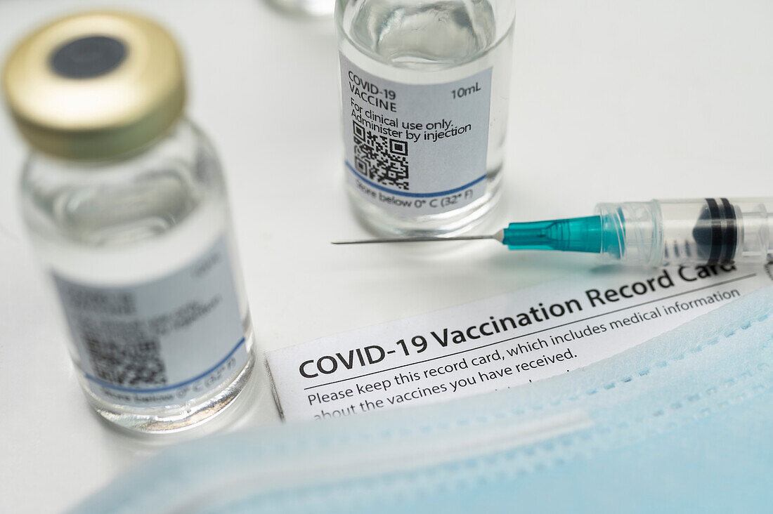 Spritze auf Covid-19-Impfpass, Gesichtsmaske und Ampulle
