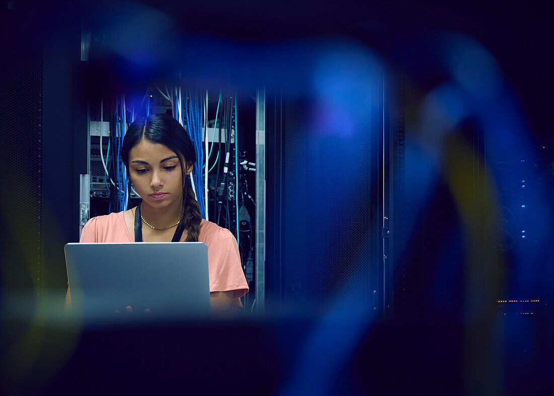 Female technician using laptop in server room