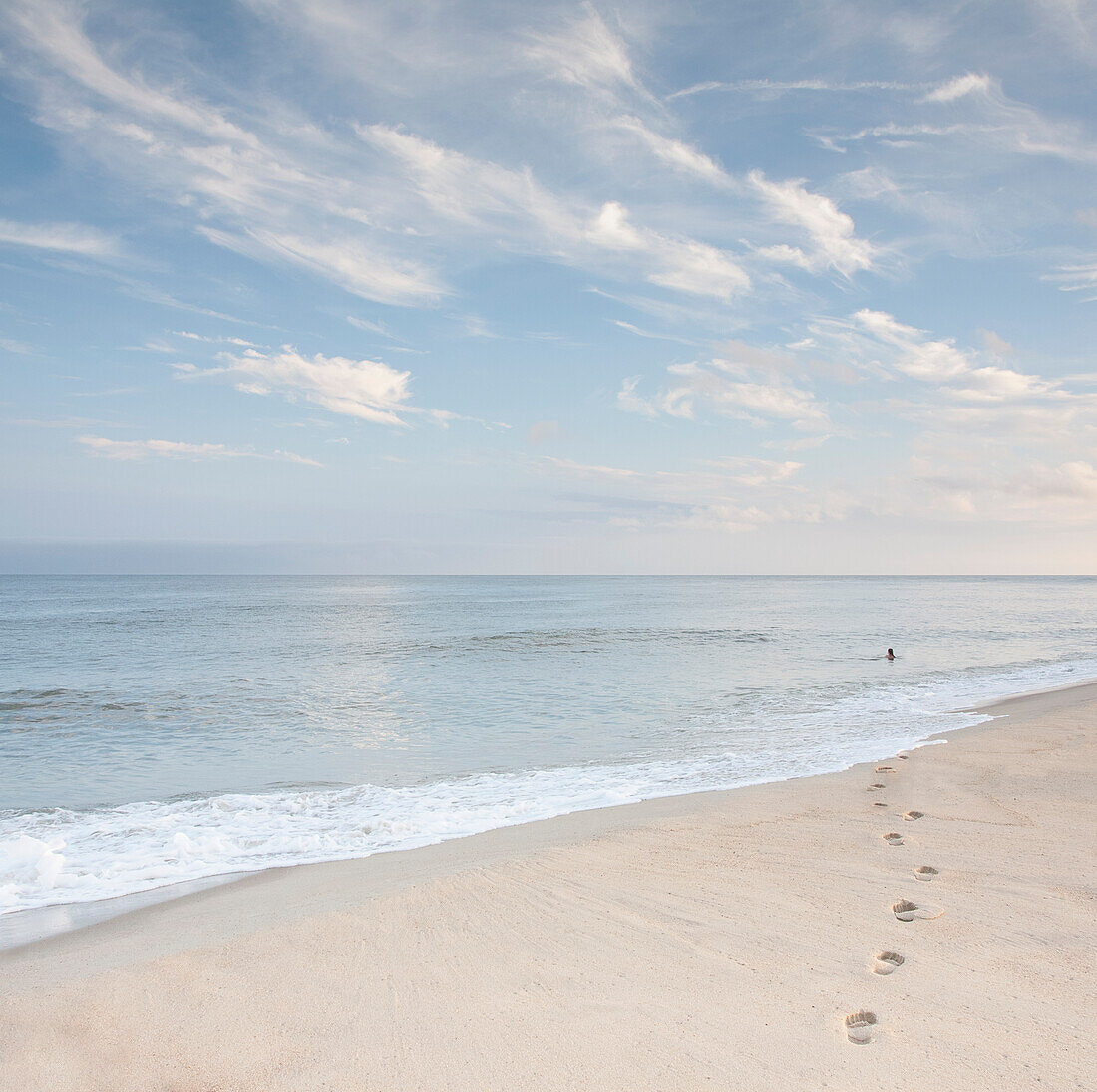 USA, Massachusetts, Cape Cod, Nantucket Island, Footprints on beach and woman swimming in ocean in distance