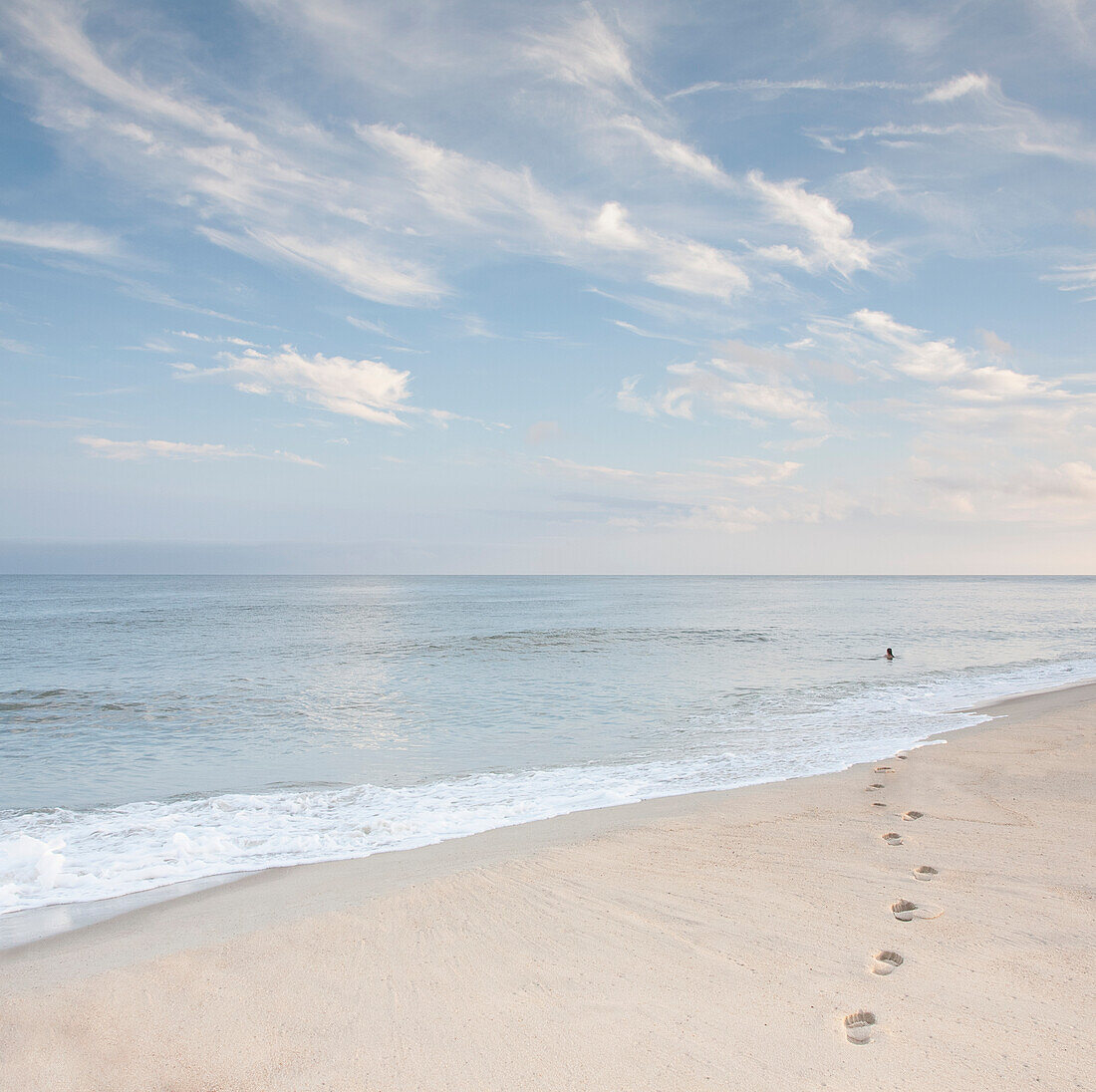 USA, Massachusetts, Cape Cod, Nantucket Island, Fußabdrücke am Strand und eine Frau, die in der Ferne im Meer schwimmt