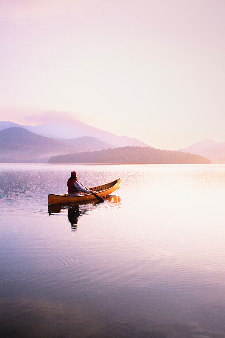 United States, New York, Woman paddling canoe on Lake Placid at sunrise, Adirondacks State Park