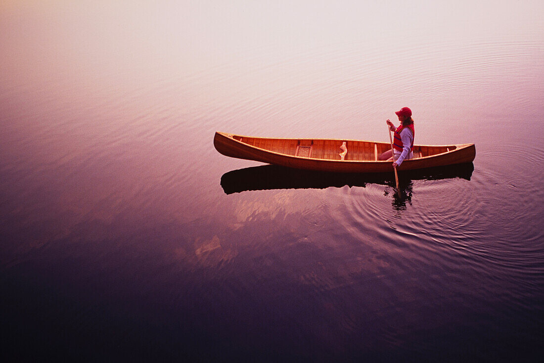 Blick von oben auf eine Frau, die bei Sonnenaufgang mit einem Kanu auf dem Lake Placid paddelt, Adirondacks State Park