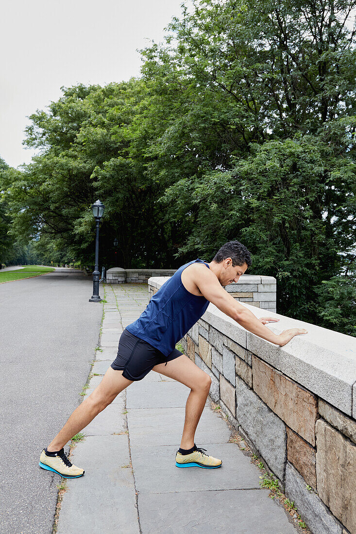 USA, New York, New York City, Mann in Sportkleidung, der sich im Park gegen eine Mauer streckt