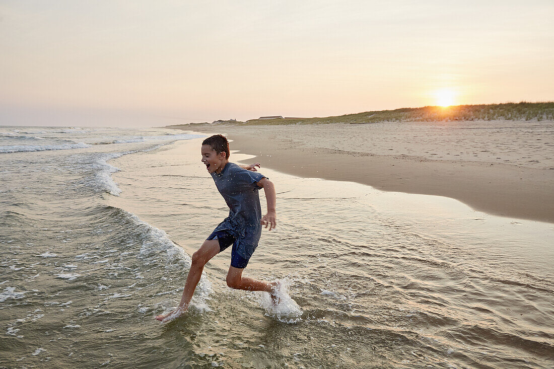 Smiling boy (8-9) playing in sea waves at sunset