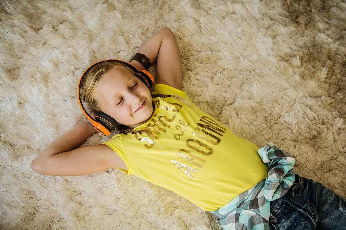 Smiling girl (10-11) with headphones lying on hairy rug with eyes closed