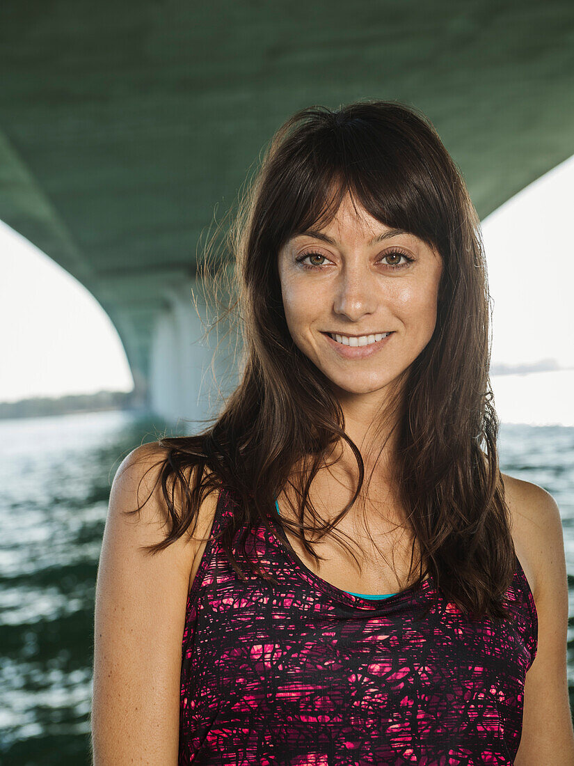 Porträt einer lächelnden Frau in ärmellosem Oberteil unter einer Brücke