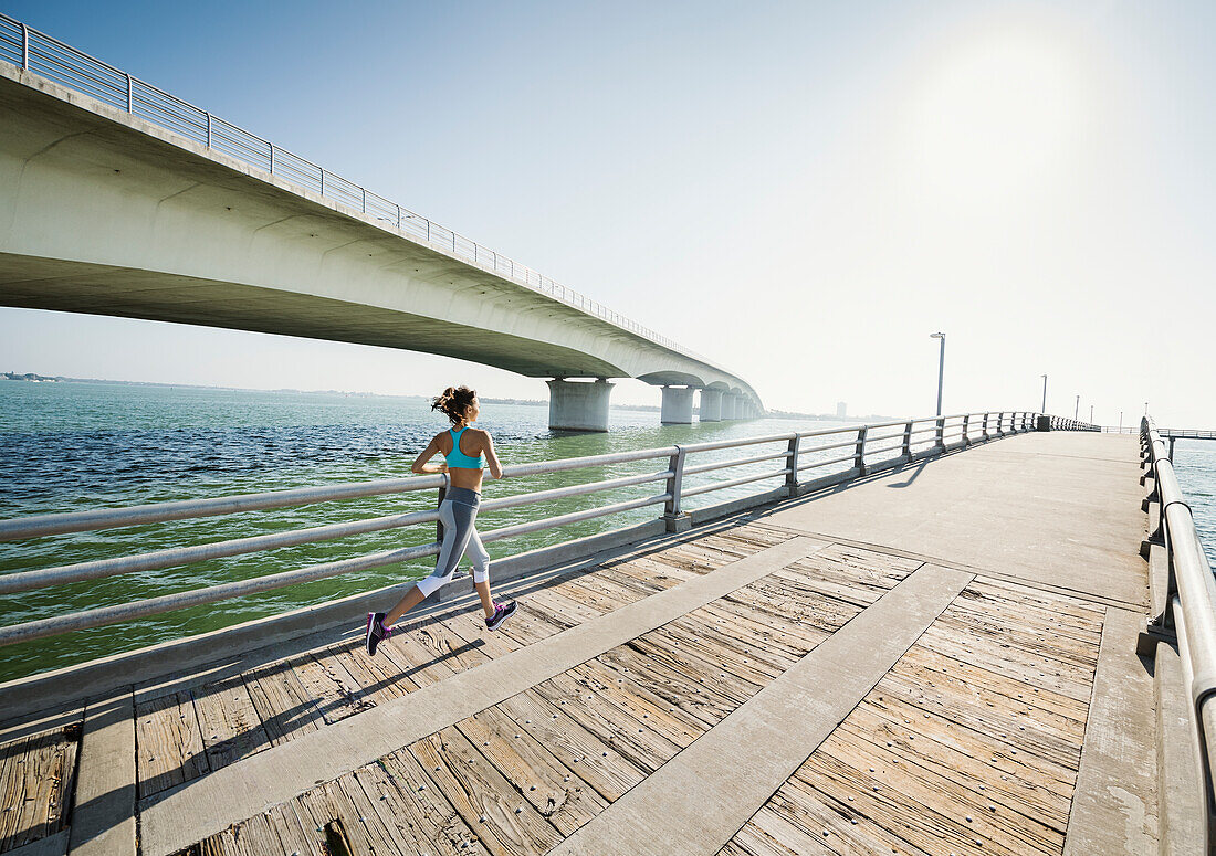 Rückansicht einer Frau beim Joggen auf einer Brücke an einem sonnigen Tag