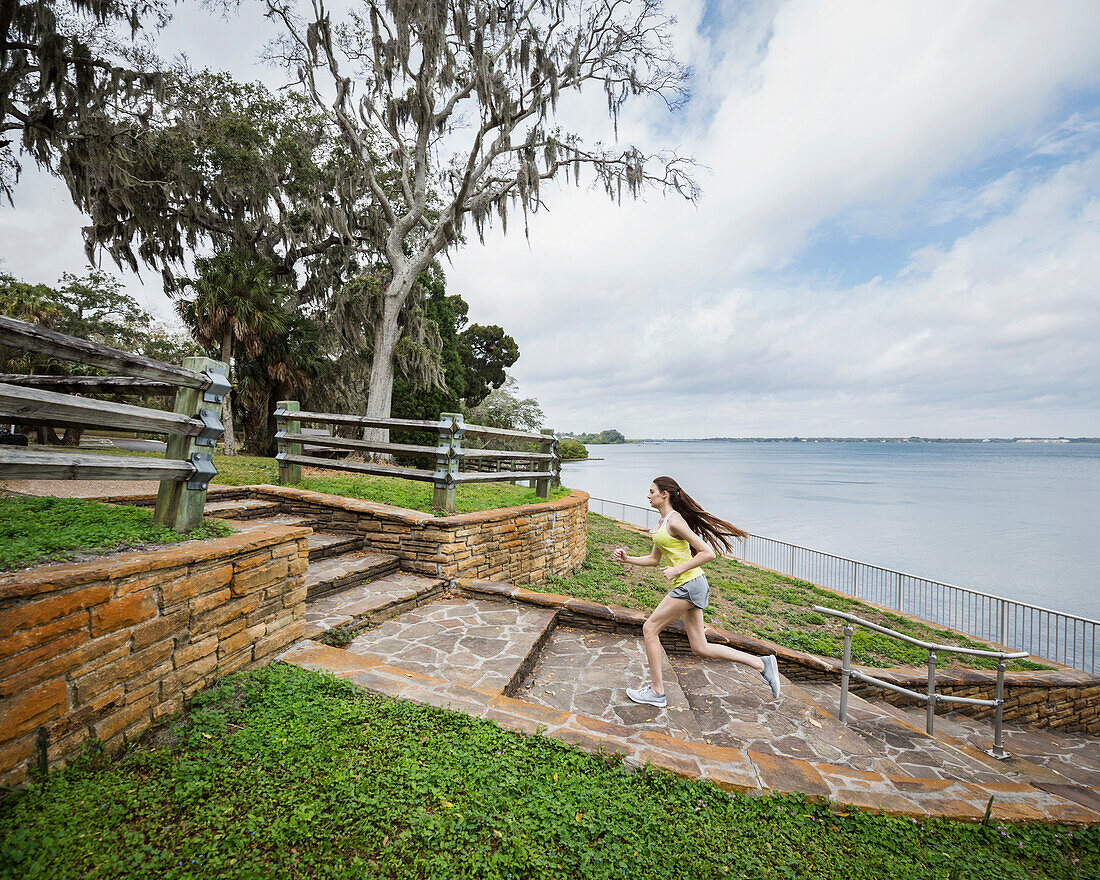 Athlete woman running up steps by river