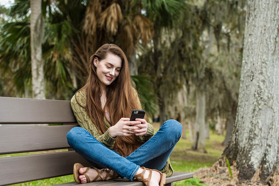 Smiling woman sitting on bench and looking at smart phone