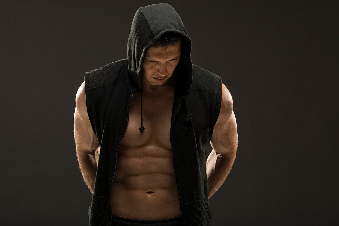 Muskulöser Mann in Kapuzenweste vor schwarzem Hintergrund