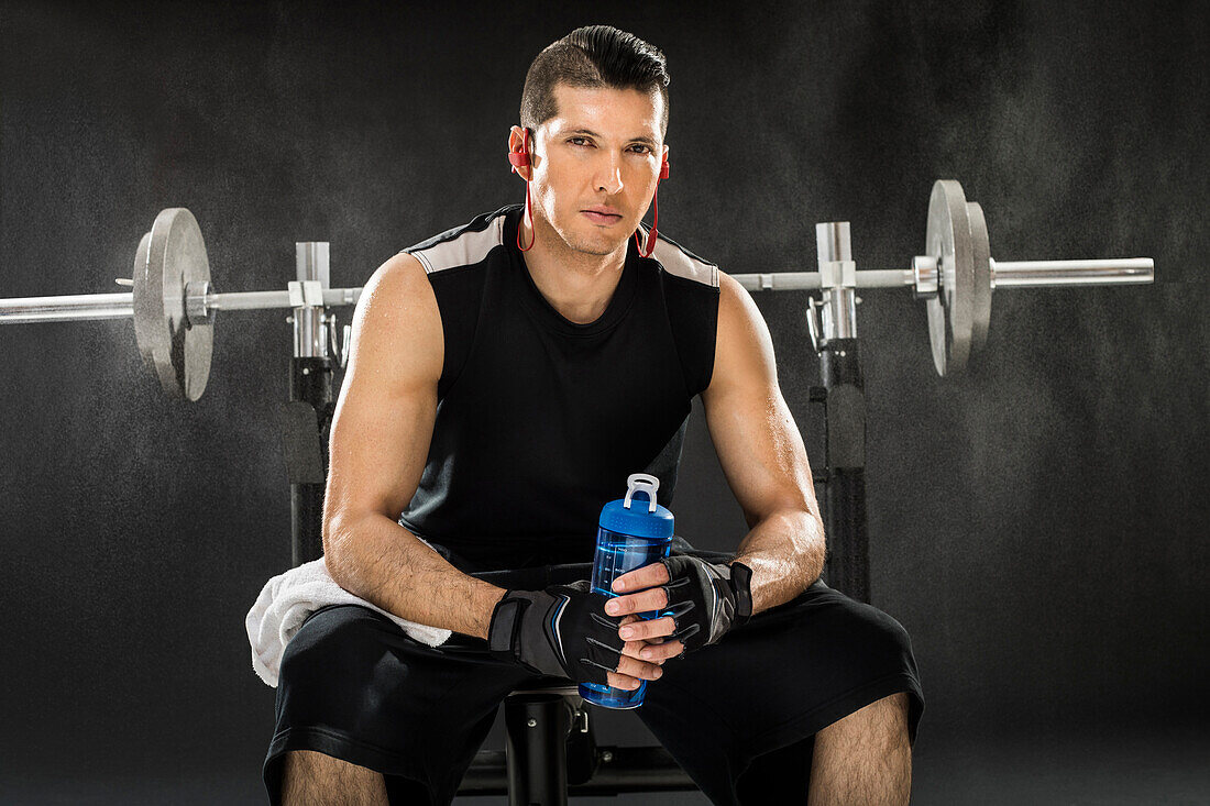 Muskulöser Mann, der mit einer Langhantel trainiert und eine Wasserflasche hält