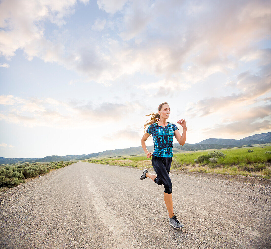 Vereinigte Staaten, Utah, Cedar Fort, Frau joggt auf der Straße in der Wüstenlandschaft