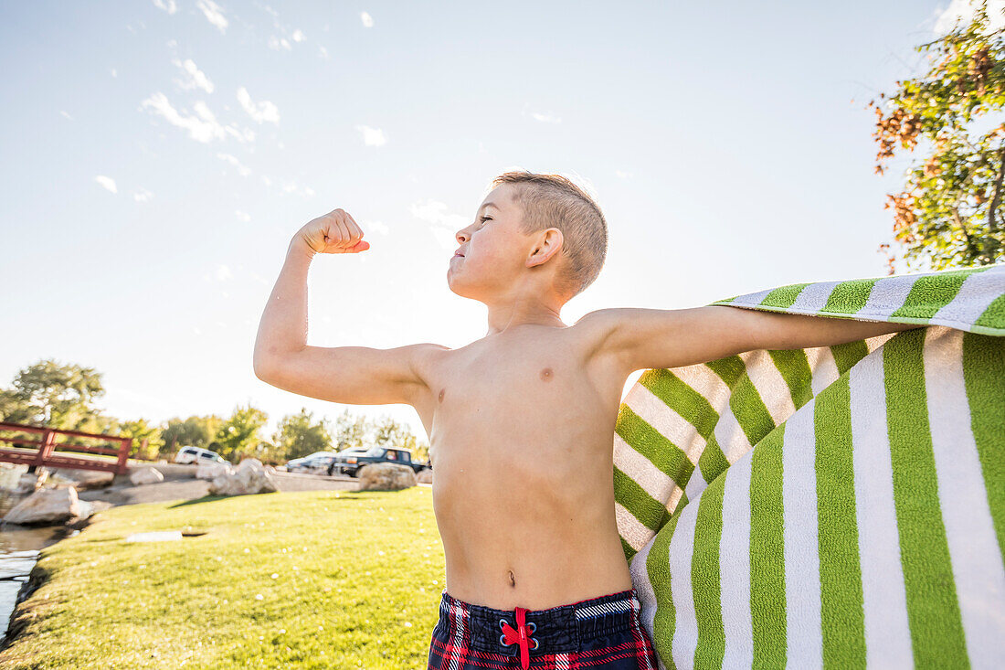 Junge ohne Hemd (8-9) lässt im Garten die Muskeln spielen