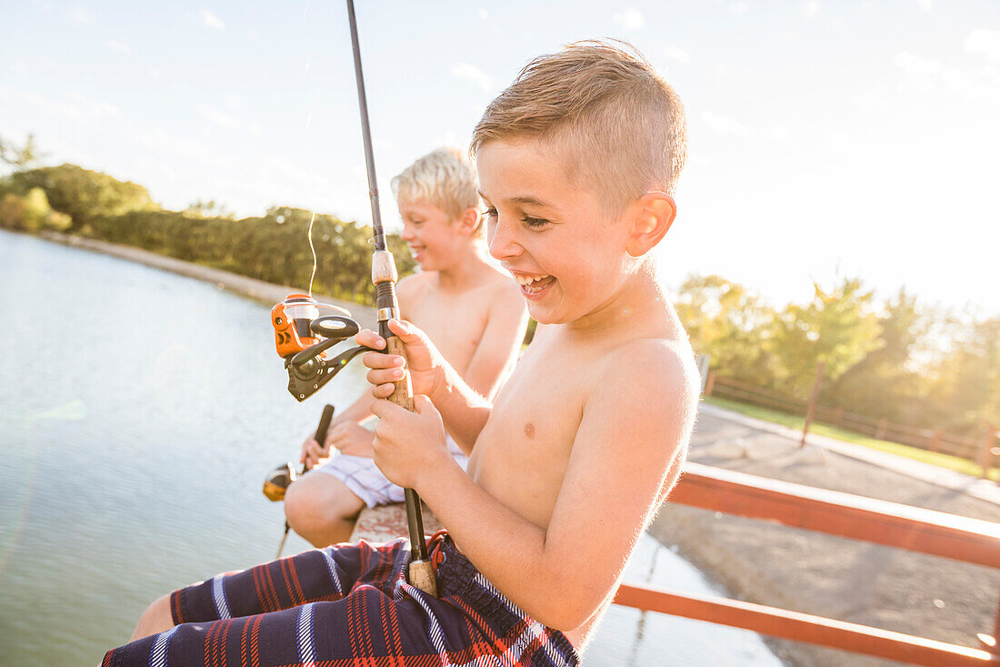 Lächelnde Jungen ohne Hemd (8-9) beim Angeln am See