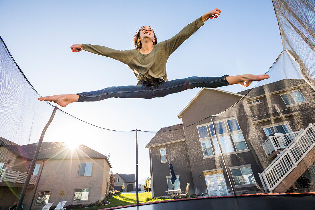 Girl (12-13) jumping on trampoline in front of house