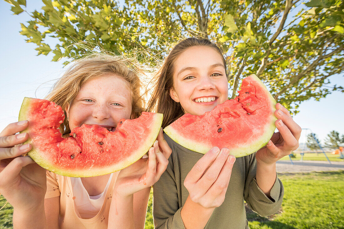 Portrait of smiling girls (10-11, 12-13) holding slices of watermelon in garden