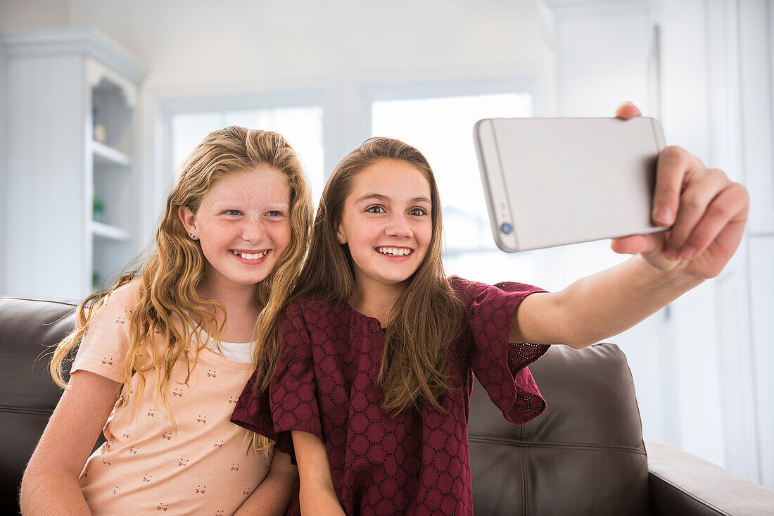 Lächelnde Schwestern (10-11, 12-13) machen ein Selfie zu Hause