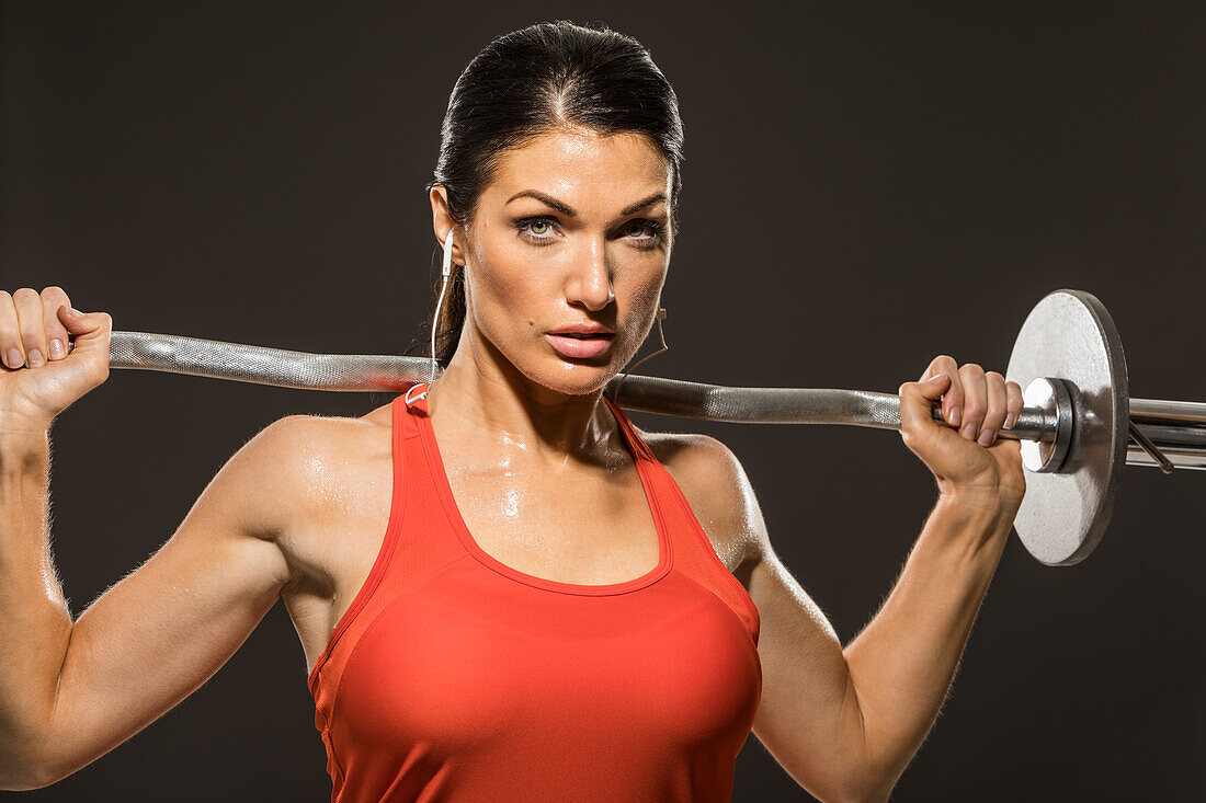 Studio portrait of athletic woman in red sleeveless top with barbell