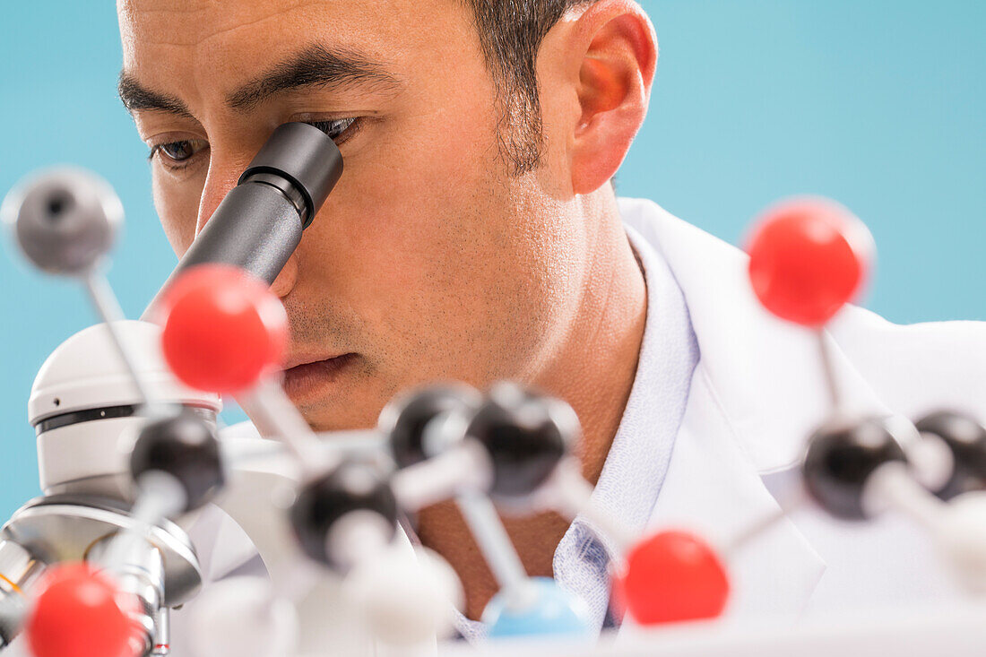 Close-up of scientist looking through microscope, molecular model in foreground