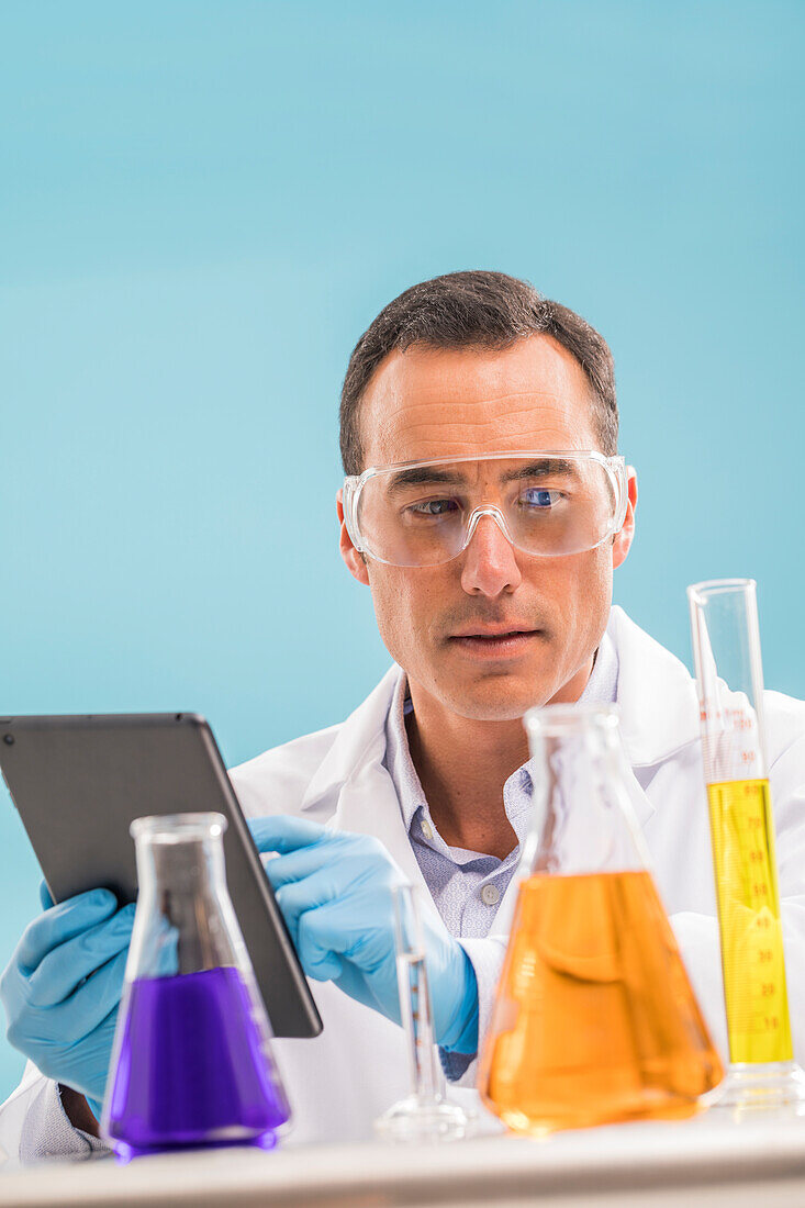 Scientist with digital tablet looking at liquids in beakers