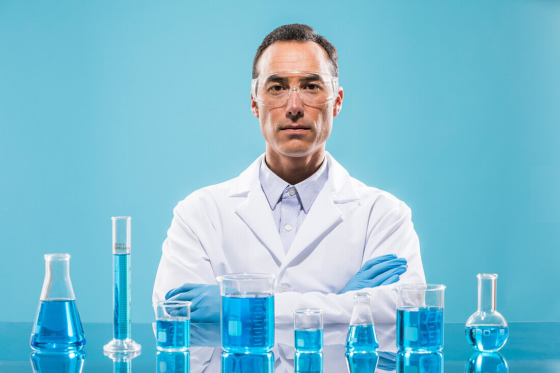 Portrait of scientist with beakers with blue liquid in foreground