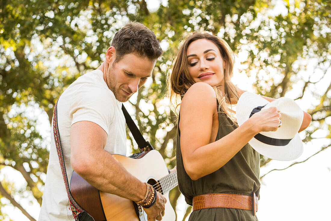 Man playing guitar and woman dancing in park 