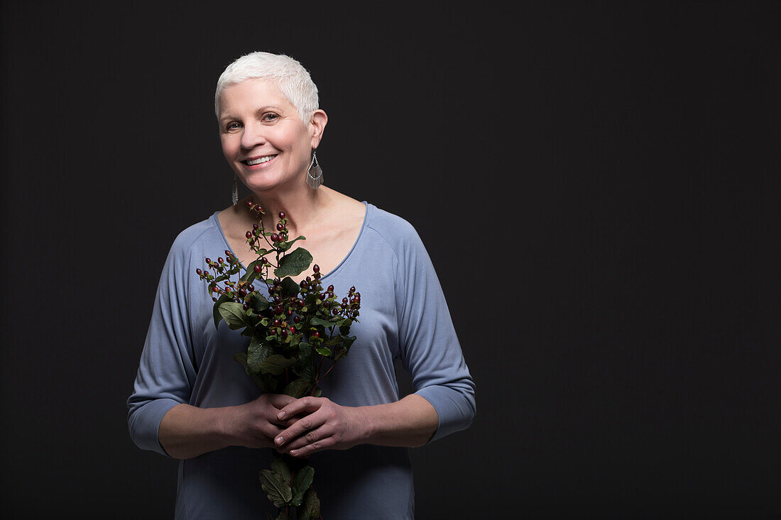 Studio-Porträt einer lächelnden Frau in blauem Hemd, die einen Blumenstrauß hält