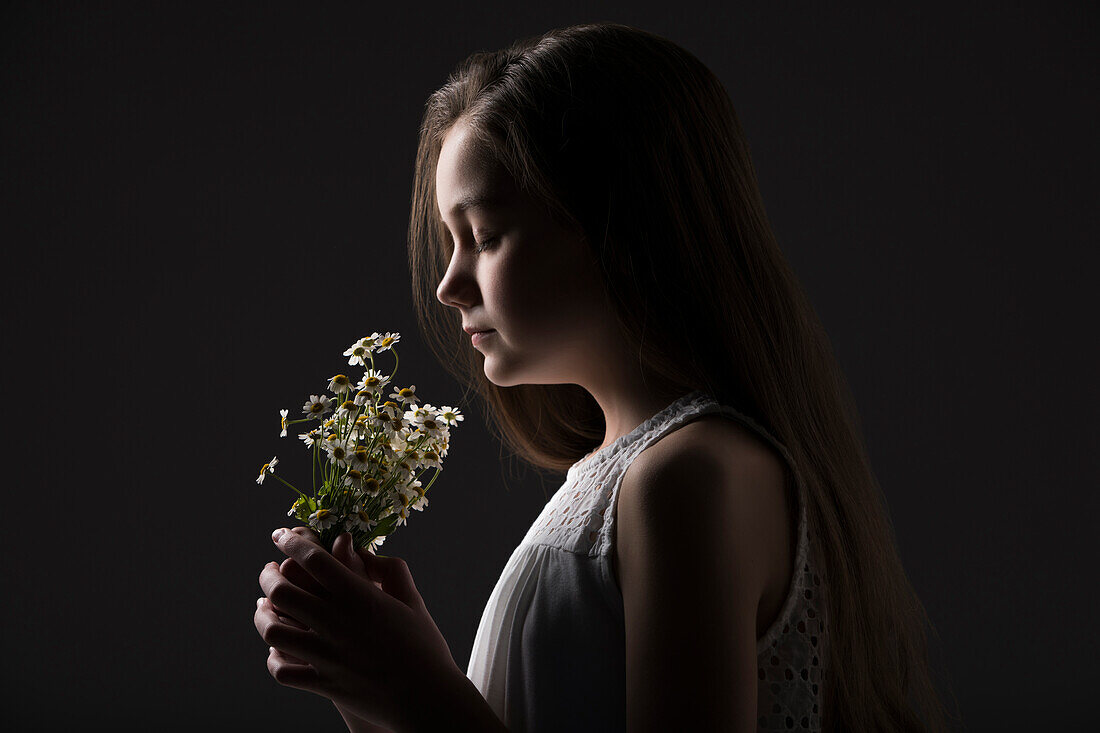 Profile of girl (10-11) holding bunch of wildflowers against black background