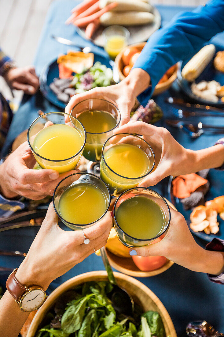 Familie mit Kindern (10-11, 12-13, 16-17) stößt mit Orangensaft an