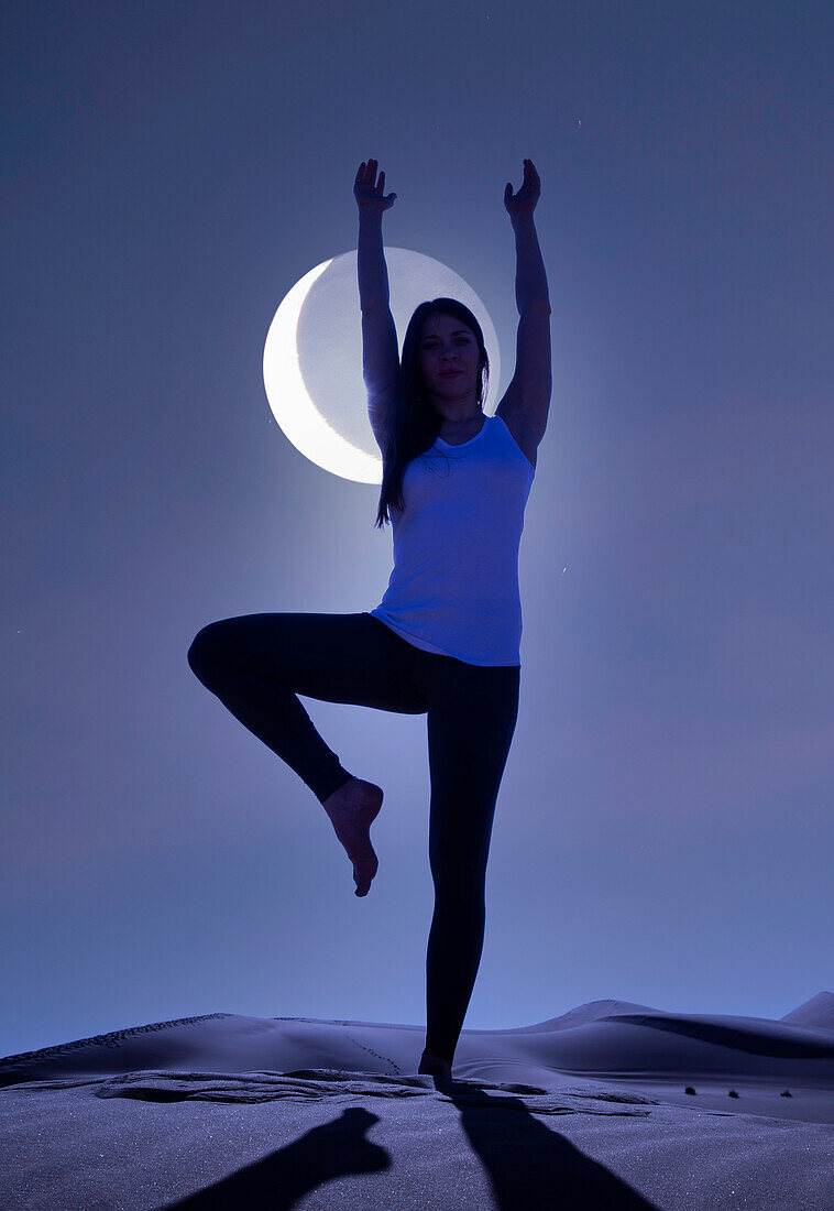 Dubai, United Arab Emirates, Woman practicing yoga on sand dune in desert at night