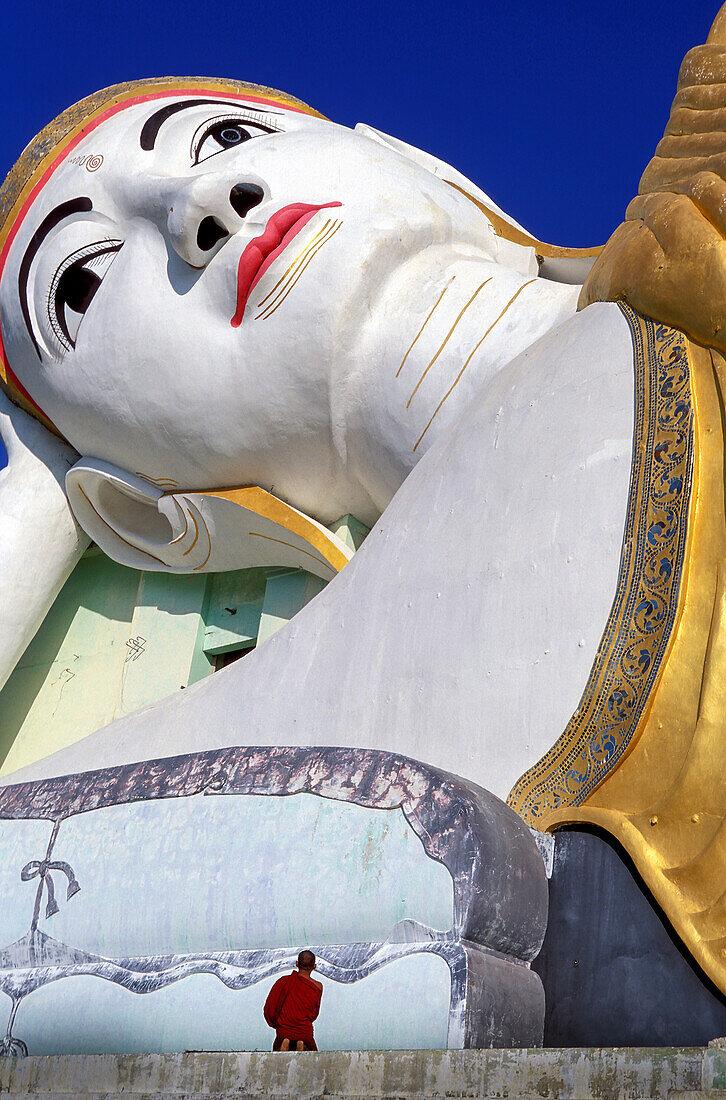 Myanmar, Monyma, Mandalay Division, Novice monk praying under giant statue of reclining Buddha in Lay Kyune Sakkyar temple