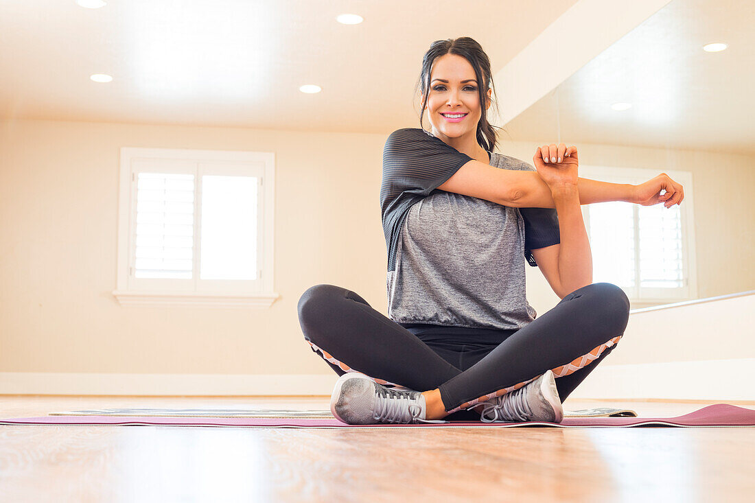 Smiling woman sitting on floor and stretching arm