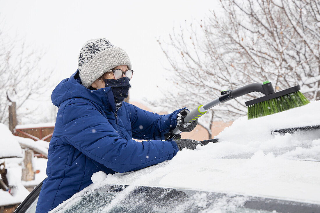USA, New Mexico, Santa Fe, Frau mit Gesichtsmaske befreit Auto von Schnee