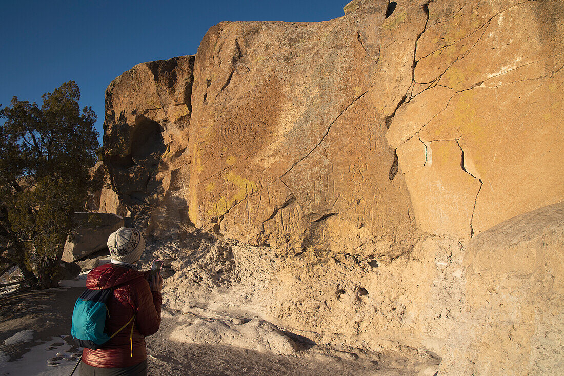 USA, New Mexico, Los Alamos, Tsankwai, Weibliche Wanderin fotografiert Petroglyphen im Bandelier National Monument