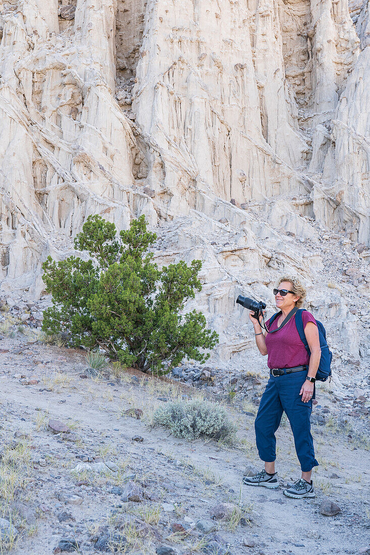 USA, New Mexico, Abiquiu, Woman with backpack and camera hiking in rocky landscape