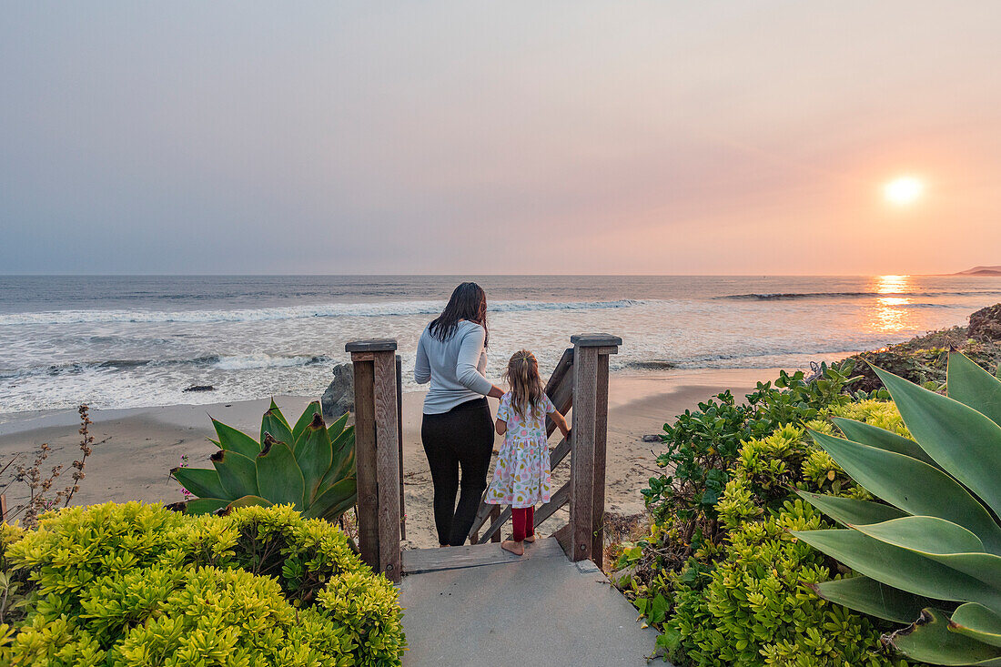 USA, California, Cayucos, Mother and daughter (4-5) on stairway to beach at sunset