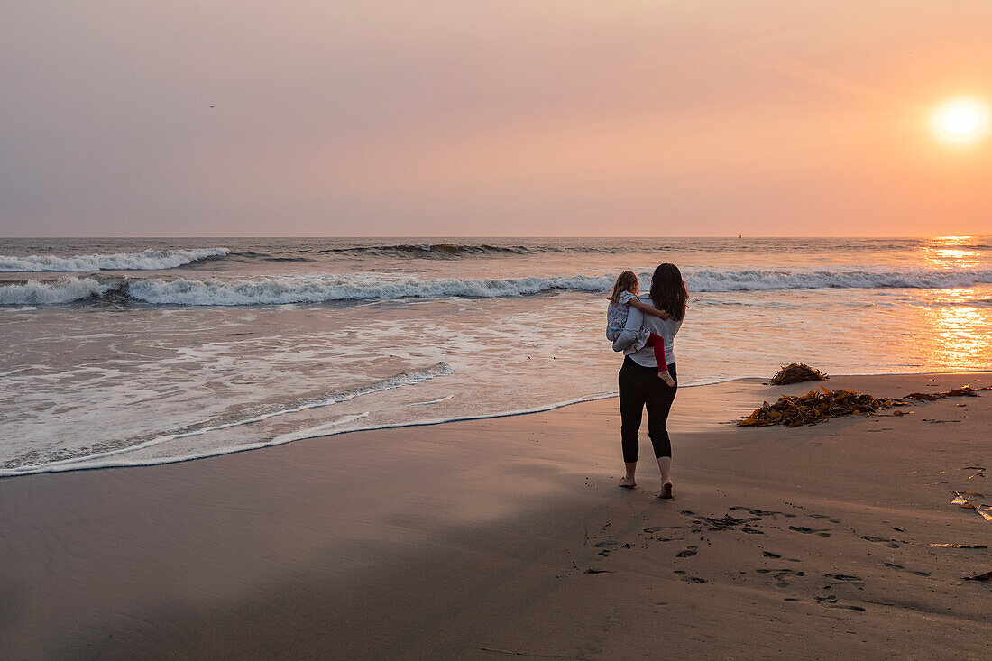 Mother and daughter (4-5) on beach at sunset