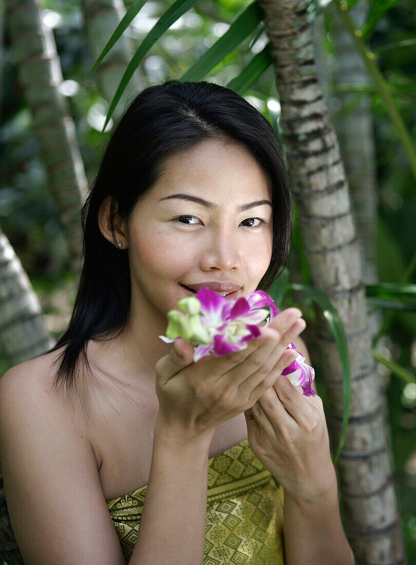 Thailand, Insel Koh Samui, Porträt einer lächelnden Frau, die an Orchideen riecht