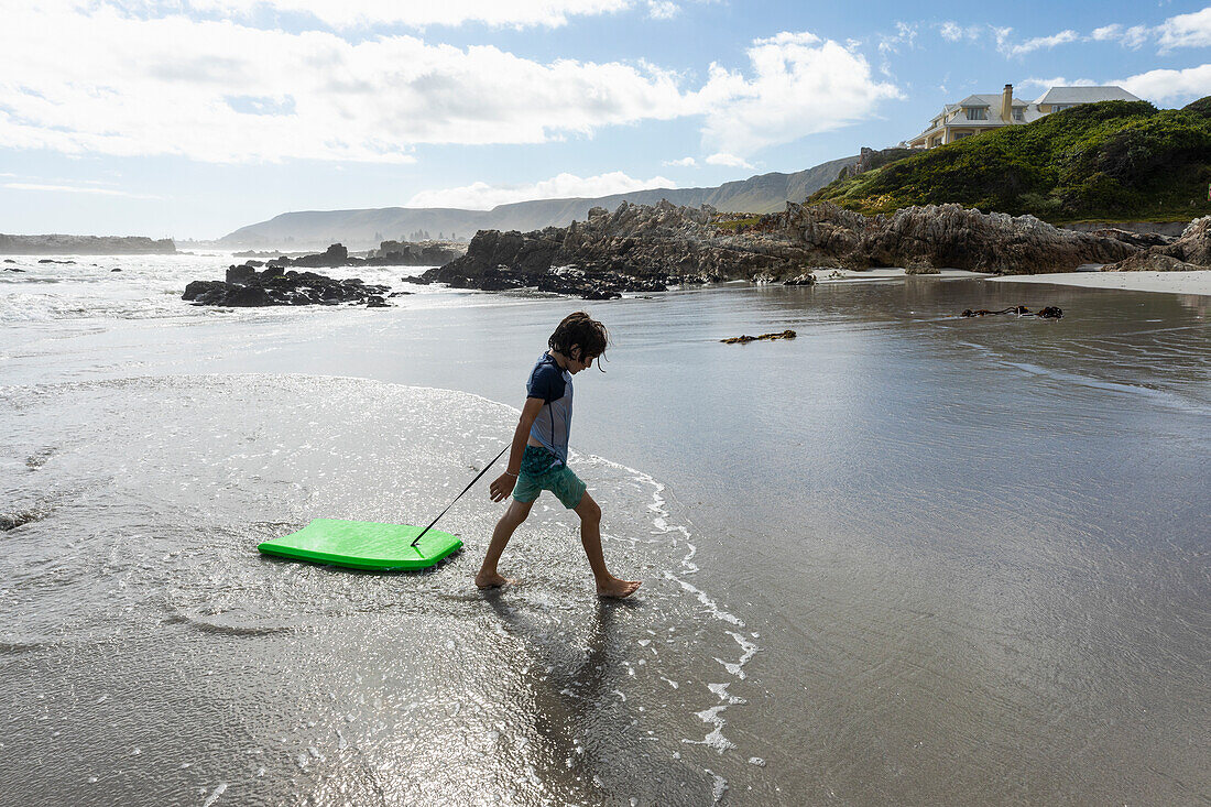 Südafrika, Hermanus, Junge (8-9) mit Surfbrett am Strand