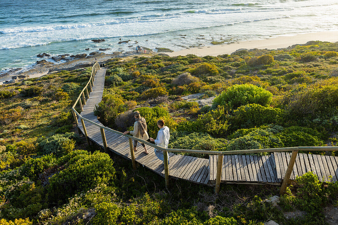 South Africa, Western Cape, Mother and daughter (16-17) walking on wooden bridge by sea in Lekkerwater Nature Reserve