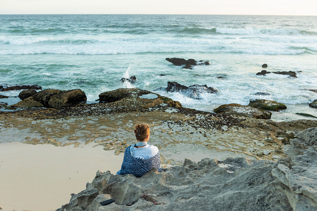 South Africa, Western Cape, Girl (16-17) sitting on beach looking at ocean in Lekkerwater Nature Reserve