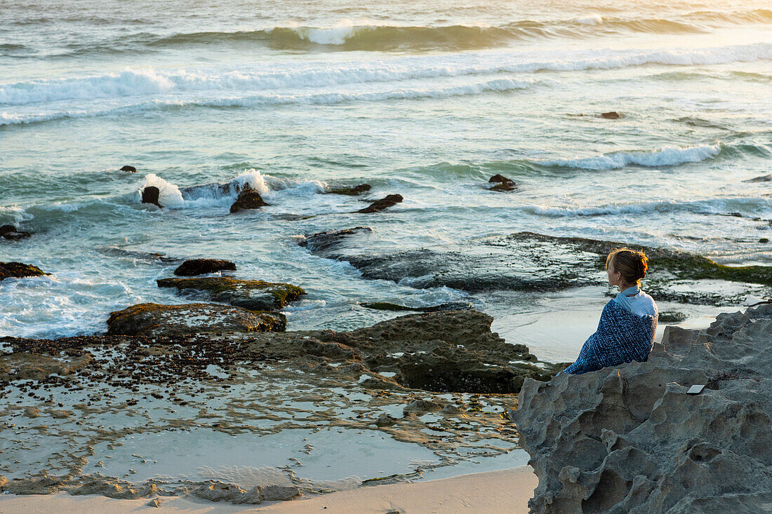 Südafrika, Westkap, Mädchen (16-17) sitzt am Strand und schaut auf den Ozean im Lekkerwater Nature Reserve