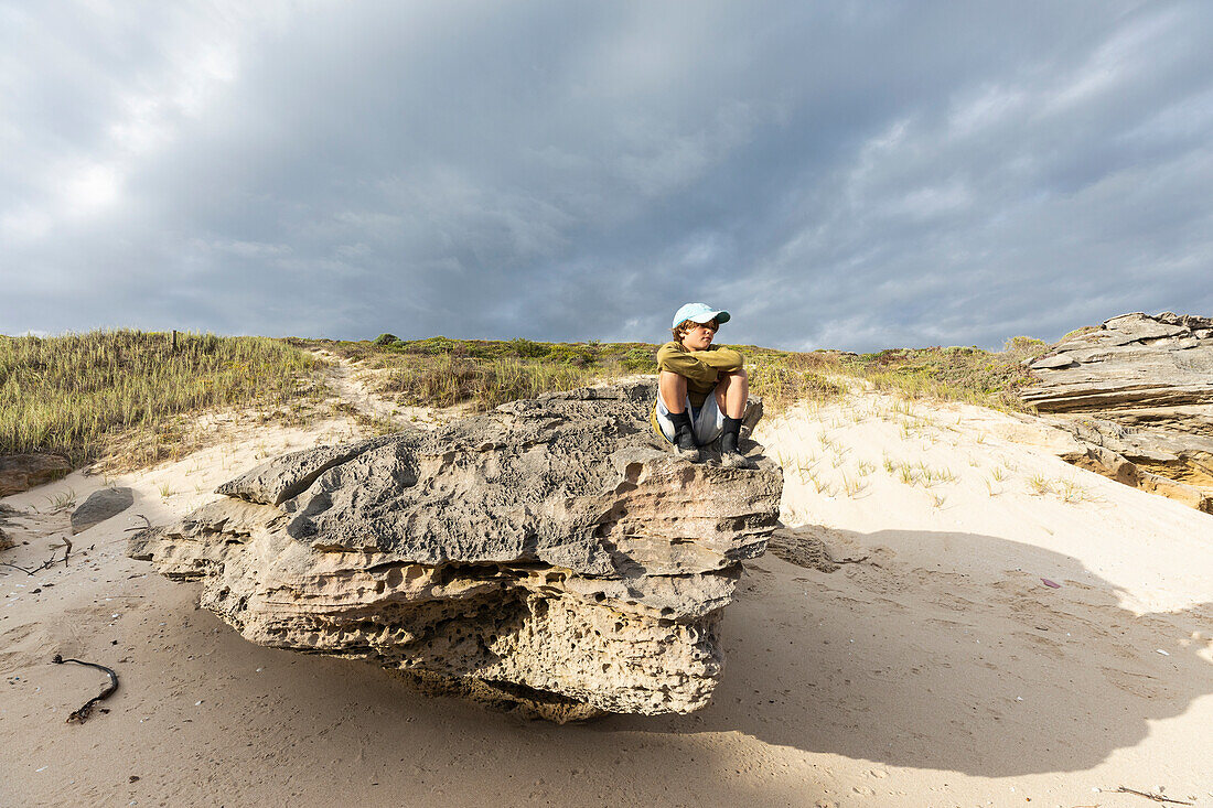 Südafrika, Westkap, Junge (8-9) sitzt auf einem Strandfelsen im Lekkerwater Naturreservat