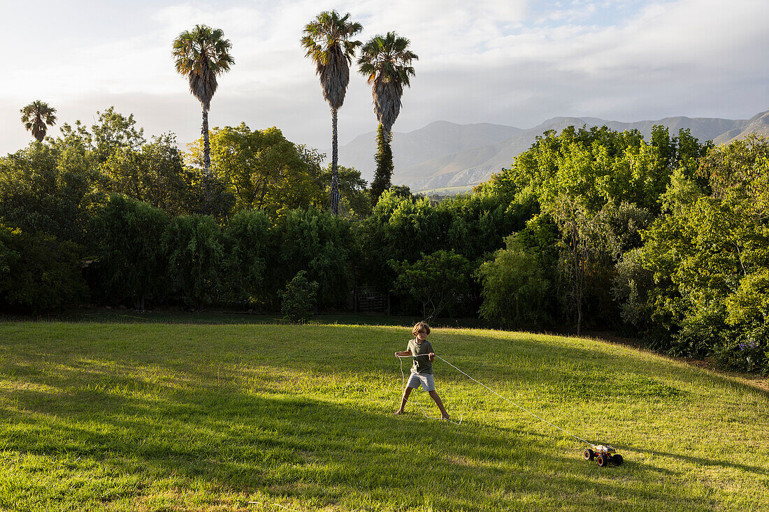 Südafrika, Stanford, Junge (8-9), der ein Spielzeugauto auf einer großen grünen Wiese zieht