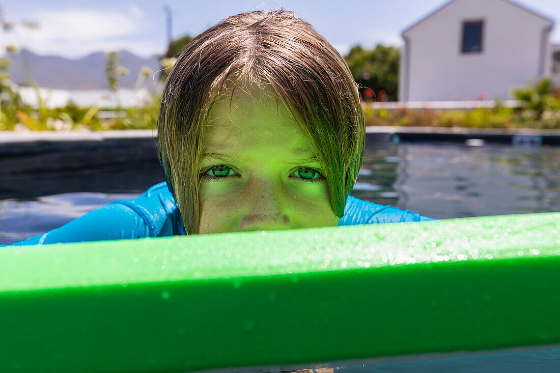 Porträt eines Jungen (8-9) auf einem grünen Bodyboard im Pool