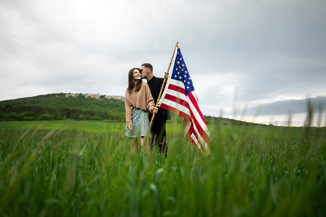 Young couple with American flag kissing in wheat field